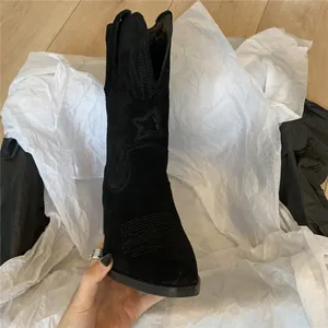Close-up of black suede western boots with star embroidery and decorative stitching.