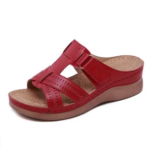 Gros plan sur des sandales compensées rouges avec motifs ajourés et détails velcro.