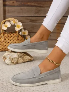 Detailansicht der grauen Wildleder-Loafer für Damen am Fuß mit goldenem Fußkettchen und Jeans.
