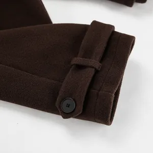 Detailopname van de mouw van een bruine wollen jas met een riempje en zwarte knoop