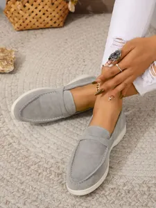 Nahaufnahme grauer Wildleder-Loafer auf einem gewebten Teppich im Lifestyle-Stil