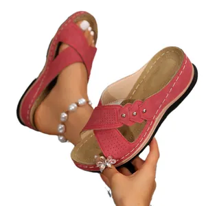 Close-up of red cross-strap wedge sandals with perforated details and flower charm