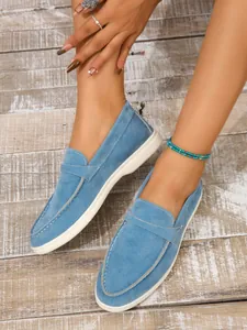 Makroansicht blauer Wildleder-Loafer mit sichtbaren Nähten auf einem Holzboden.