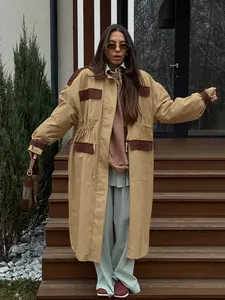 Full body view of an oversized khaki barn coat with brown contrast panels on stairs.