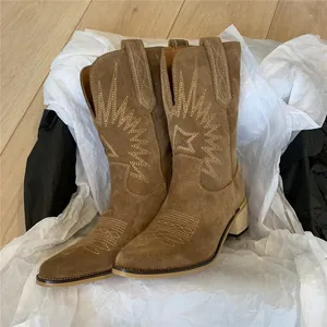Detail view of brown suede western boots with retro embroidery on white tissue paper