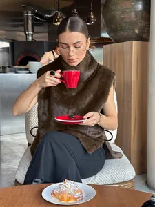 Donna elegante che indossa un gilet di pelliccia sintetica marrone a collo alto in un caffè