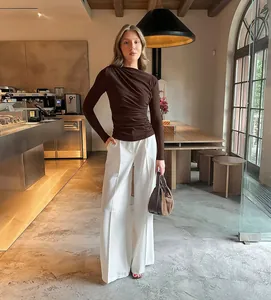 Bruine aansluitende top met rimpels en lange mouwen en witte wijde broek in café