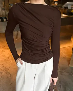 Detail van het geplooide ontwerp op een donkerbruine nauwsluitende top met mouwen