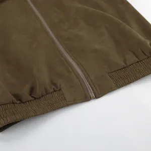 Close-up van een kaki suède jas met metalen ritssluiting en een elastische zoom onderaan.