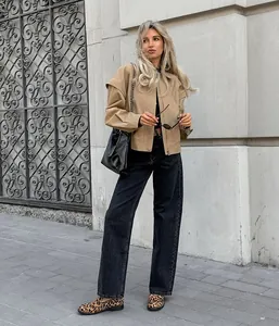 Frau in khakifarbenem Mantel mit Revers und schwarzer weit geschnittener Jeans in der Stadt