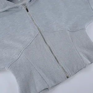 Detalle de sudadera gris con capucha, cintura de punto acanalado y cremallera frontal