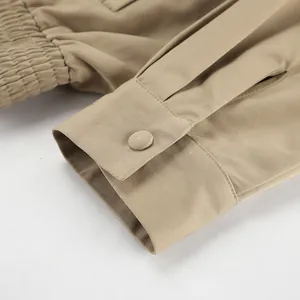 Detailaufnahme eines khakifarbenen Trenchcoats mit Knopfmanschette und Stoffstruktur.