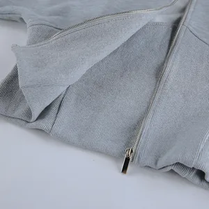 Primer plano de sudadera gris con cremallera plateada y detalle de cintura acanalada.