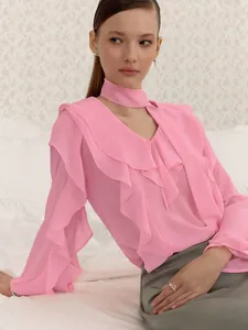 Detalle de blusa rosa con cuello en V y volantes, cuello choker y mangas con capas suaves.