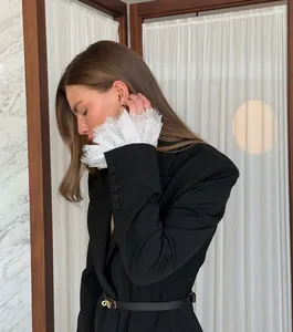Detail of black blazer featuring delicate white lace cuffs and a thin waist belt.