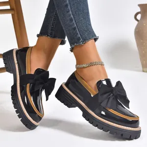 Side view of black patent leather loafers featuring a large bow and thick lug sole