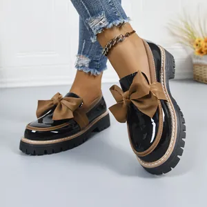 Close-up detail of women's black patent leather loafers with a large brown bow