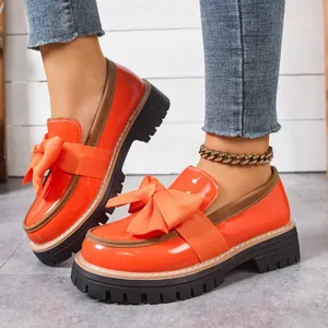 Close-up of vibrant orange patent leather loafers with large bows and thick lug soles