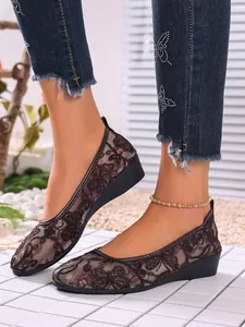 Close-up of breathable brown lace mesh flat shoes with elegant floral pattern on model.