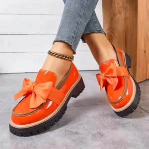 Detail view of orange patent leather loafers with large bow and thick lug sole.
