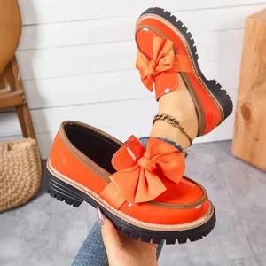 Close-up of bright orange patent leather loafers featuring a decorative oversized bow