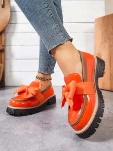 Stylish orange patent leather loafers with large bow and chunky black platform sole.