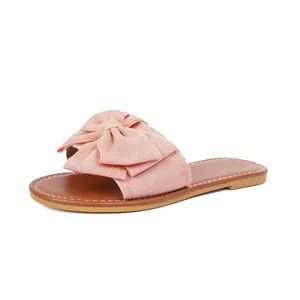 Detail view of pink bow slide sandal featuring a brown flat sole and white stitching