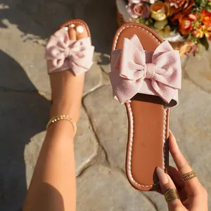 Close-up of pink fabric bow flat slippers with brown sole and white stitching detail.