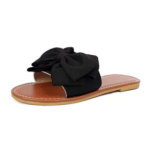 Close-up of black fabric bow detail on stylish flat slide sandal with brown sole.