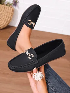 Close-up detail view of black textured loafers with gold butterfly ornament on model