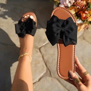 Close-up of women's flat slippers with a large black fabric bow and brown insole