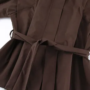 Detailaufnahme des Bindegürtels und des Faltenstoffs an einem braunen Trenchcoat