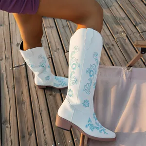 Detail shot of white knee-high cowboy boots featuring blue floral embroidery on a deck
