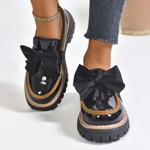 Women's chic black patent leather loafers featuring large bow and thick platform sole.
