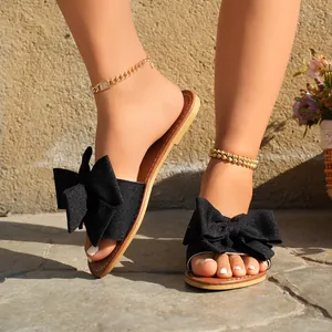 Close-up detail of women's black flat slippers featuring a large elegant bow knot