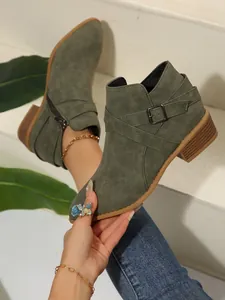 Detailed view of olive green pointed-toe Chelsea boots with cross straps and buckle