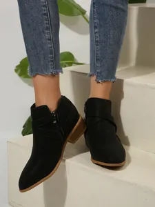 Detail view of black pointed toe Chelsea boots with cross straps and side zipper.