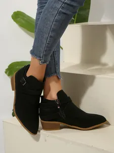 Close-up detail of black pointed-toe Chelsea boots featuring cross straps and side zipper