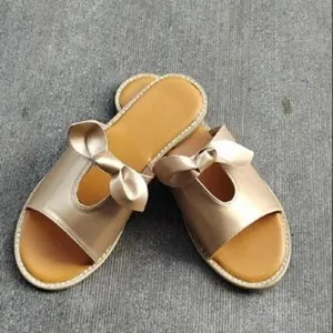 Close-up of golden flat slippers for women featuring a stylish bow decoration on wide straps