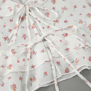 Primer plano de una blusa de gasa con flores blancas, detalle de lazo y bordes volantes