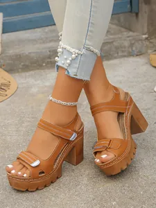 Close-up of women's brown platform chunky heel sandals with pearl-trimmed denim jeans.