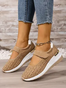 Detail view of beige laser-cut sneakers with wedge sole and velcro strap on foot