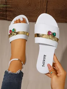 Detail view of white flat slide sandals decorated with colorful heart-shaped gem accents.