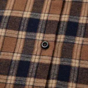 Close-up detail of brown plaid flannel fabric with a black button on a casual shirt.