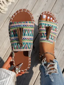 Detalle de sandalias planas bohemias con estampado tribal y borla sobre fondo de madera