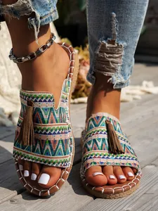 Primer plano de sandalias planas tejidas estilo bohemio con borlas sobre madera