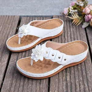 Detailed view of white wedge thong sandals with a decorative flower and metal studs