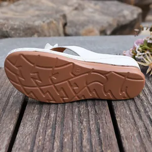 Detail view of the durable non-slip brown rubber sole of a white wedge sandal shoe