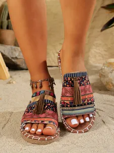 Sandalias bohemias planas con patrones coloridos y borlas en fondo de playa de arena