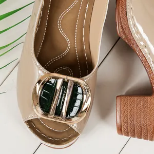 Close-up of beige peep-toe high heel sandal with elegant gold and green buckle
